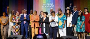 Homens e mulheres negras em cima de um palco, sorrindo, comemorando o lançamento de um prêmio.